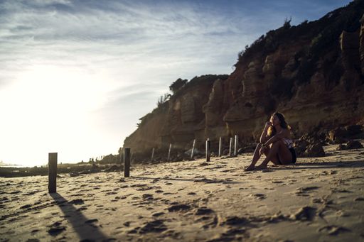 A young female in swimsuit sitting on sands on background of a cliff