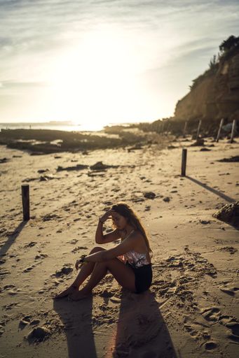 A young female in swimsuit sitting on sands on background of a shore