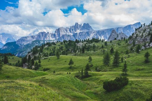 A low angle shot of a greenfield surrounded by mountains under the cloudy sky in Dolomites, Italy