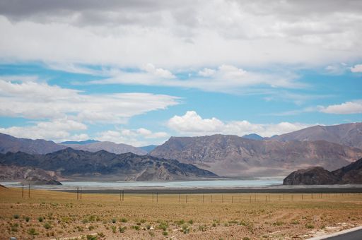 A wide field with a small lake and mountains behind the fencing in the background under the cloudy sky
