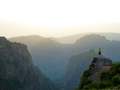 A beautiful shot of a male standing on the edge of a cliff overlooking shaded mountains below