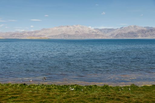 A scenic view of a crystal blue lake surrounded by towering mountains on a bright sunny day
