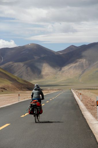 A human riding bicycle on road through desert surrounded by hills