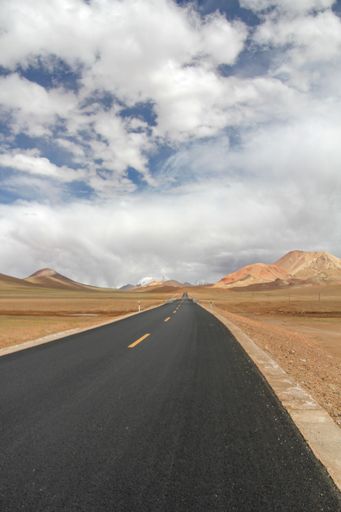 A landscape with a road and mountains against the sky with floating clouds