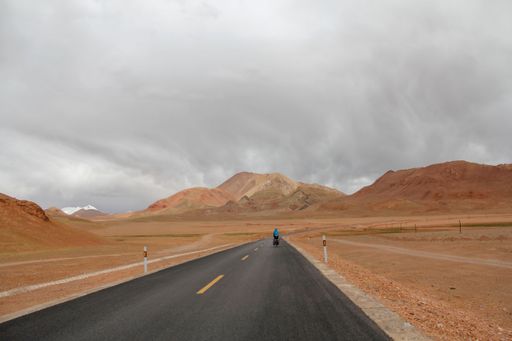 A landscape with a motorcyclist on road and mountains against the sky with floating clouds