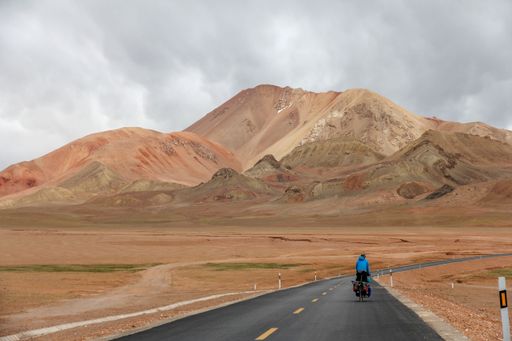 A human riding bicycle on road through desert surrounded by mountains
