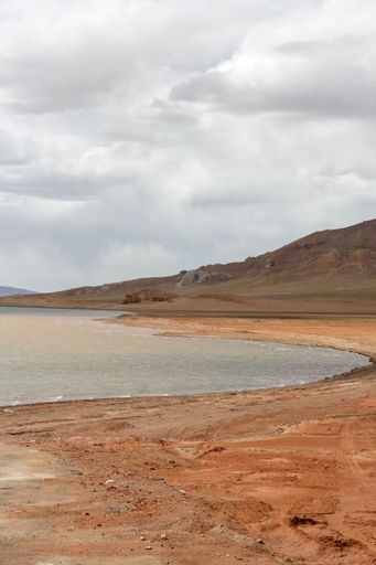 A landscape with a lake and mountains against the sky with floating clouds