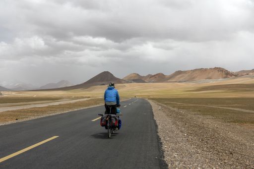 A human riding bicycle on road through desert surrounded by mountains
