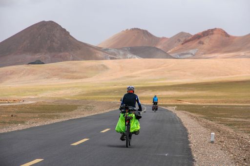 A human riding bicycle on road through desert surrounded by mountains