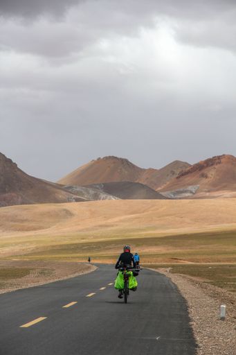 A human riding bicycle on road through desert surrounded by mountains