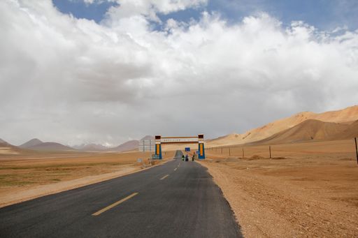 A human riding bicycle on road through desert surrounded by mountains
