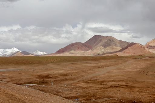 A landscape with a rocky dirt ground and mountains against the sky with floating clouds