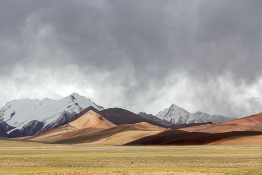 The beautiful mountains with some covered in snow in a green field against the sky