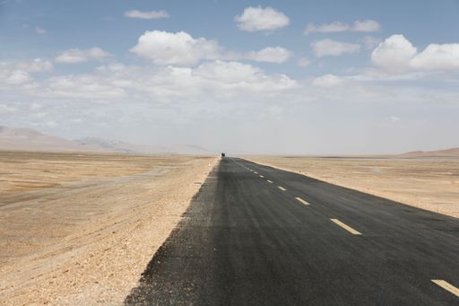 A landscape with a road and mountains against the sky with floating clouds