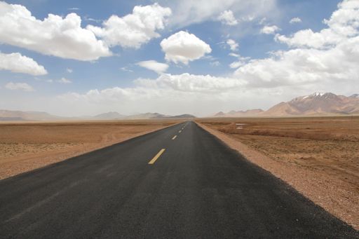 A landscape with a road and mountains against the sky with floating clouds