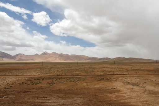 A landscape with mountains and bushes against the sky with floating clouds