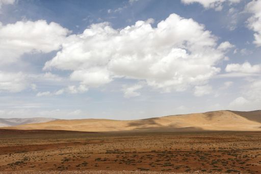A landscape with mountains and bushes against the sky with floating clouds