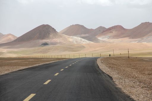 A landscape with a motorcyclist on a road and mountains against the sky