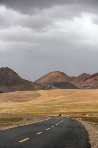 A landscape with a road and mountains against the sky with floating fog clouds