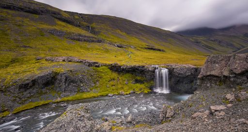 A beautiful shot of a mountainous landscape with a small waterfall with an overcast sky