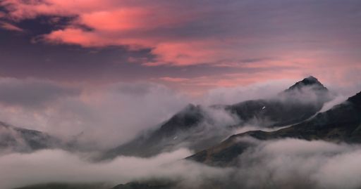 A beautiful shot of mountaintops covered in clouds with the evening pink sunset illuminating the sky