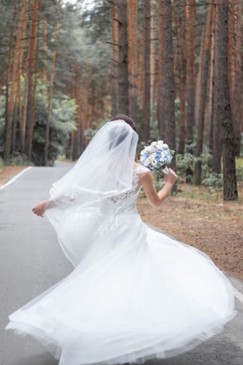 A vertical back view of a bride in white dress running with a bouquet in a park