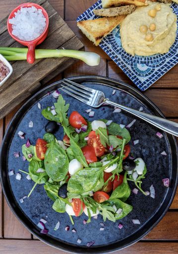 A vertical shot of a green salad with hummus on the side on a wooden table