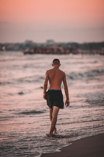A vertical shot of a man walking on a beach in the sunset