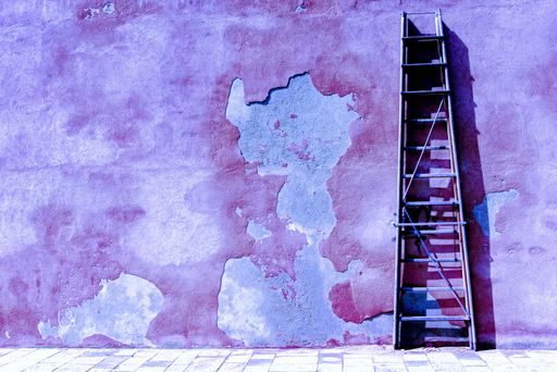 A horizontal image of a wooden ladder against a purple old wall