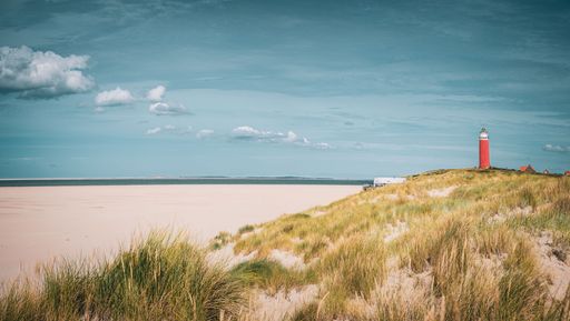 A red lighthouse on a hill covered with grass and a sandy beach in the background