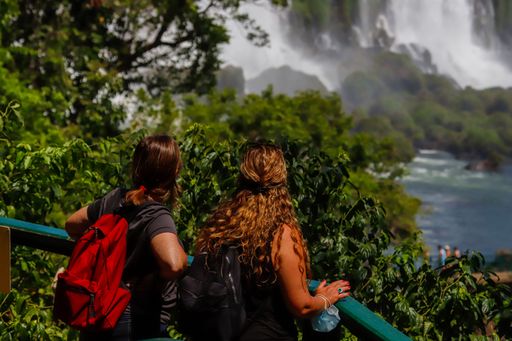A back view of a pair of female tourist friends looking at the Iguazu Falls together