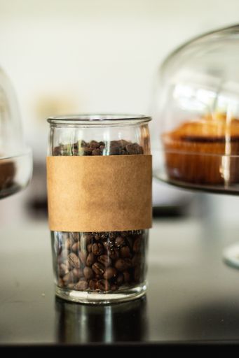 A vertical shot of a container full of coffee beans with cupcakes in the background