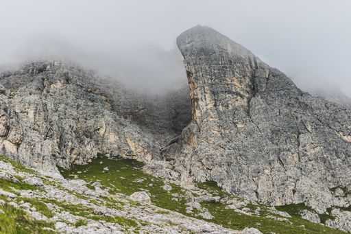 A rock formation covered in fog in the middle of mountainous scenery in Dolomites, Italy