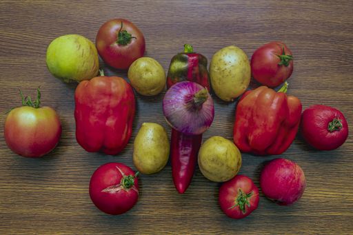 A top view of red bell peppers, onions, potatoes and tomatoes laying on the kitchen table