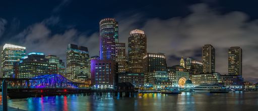 A panoramic shot of a cityscape with a lot of illuminated buildings near the sea under the breathtaking sky