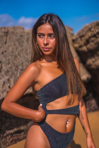 A vertical shot of an attractive female in a sexy swimsuit posing on the beach near the rocks