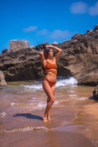A vertical shot of a female in a bikini posing on the beach near the rocks