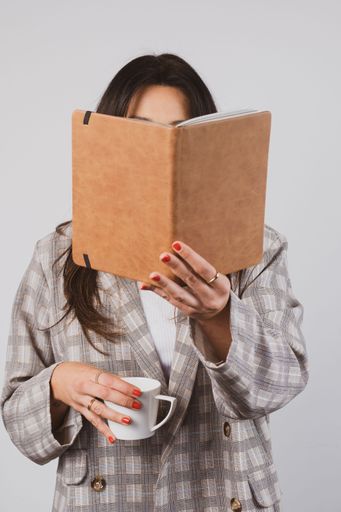 A vertical shot of a woman reading a book while drinking coffee when standing up
