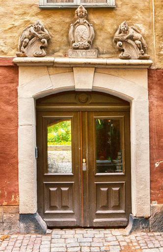 A vertical shot of an old wooden door with a stone arch and statues on it, The Old Town, Stockholm