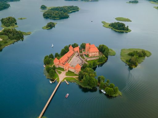 An aerial shot of the Trakai castle surrounded by green trees over the Galves lake in Trakai, Lithuania