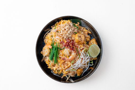 A top view of Thai noodles made with shrimp, sprouts, peanuts and flakes on a white background