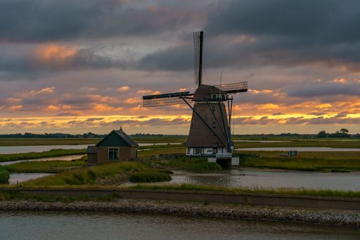 A dramatic shot of the Kagerplassen windmill and a barn during sunset with a pinkish sky