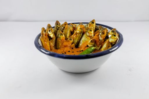 A closeup of Indian carplet fish cooked in yellow gravy in a white ceramic bowl on a white background