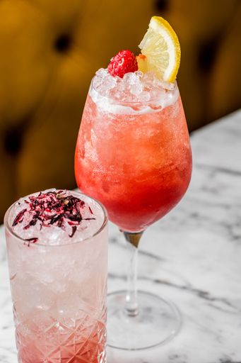 A vertical shot of a raspberry cocktail with lime and ice on a stone table