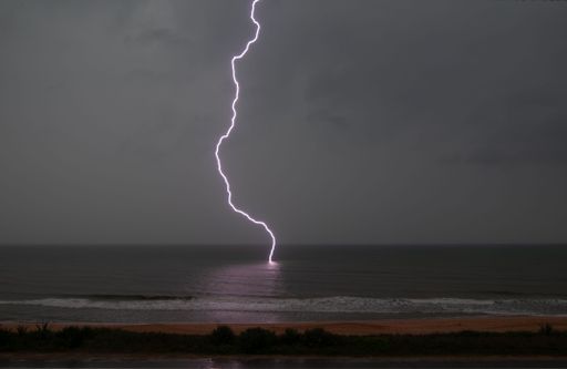 A bolt of lightning hitting the open sea surface near the beach during a night
