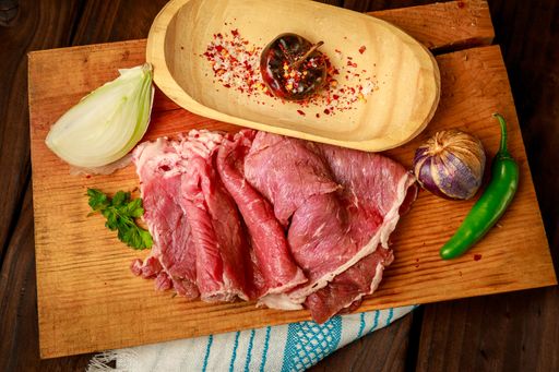 A top view of a cherry in a bowl and corned beef slices with vegetables on a wooden cutting board