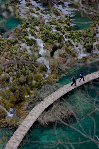 A high angle shot of people with backpacks walking on a wooden trail on a river