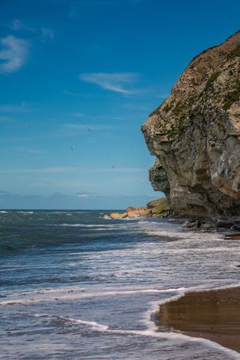 A vertical shot of a wavy ocean with rocky cliffs on the beach