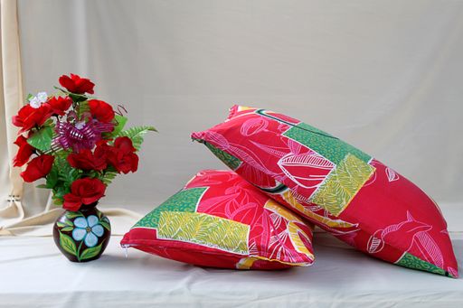 A closeup shot of colorful pillow and flowers in a vase isolated on a pink background