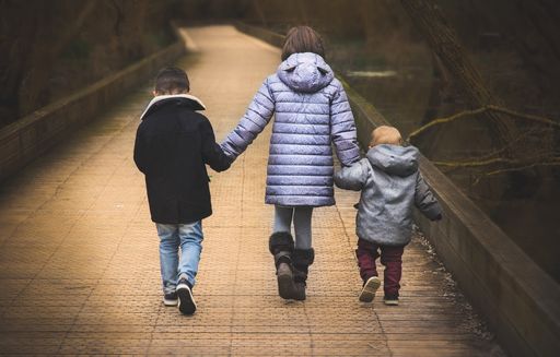 A back view of three kids holding the hands of each other and walking on a bridge